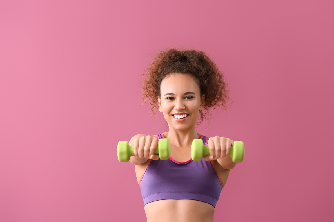 Young Woman Using Dumbbells on Pink Background